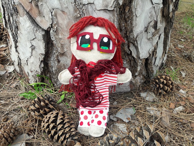 A red-haired and green-eyed plush doll wearing a red and white outfit with a frilly red scarf and glasses.