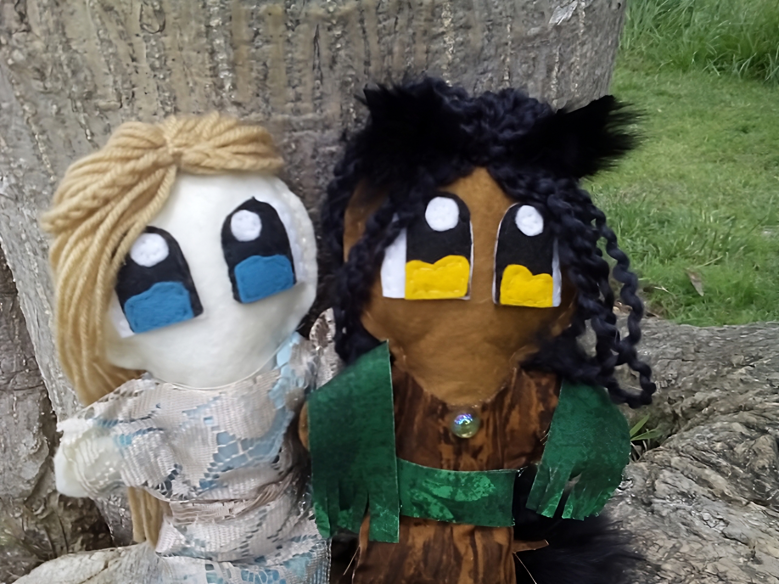 Two plush dolls stand at the base of a tree.